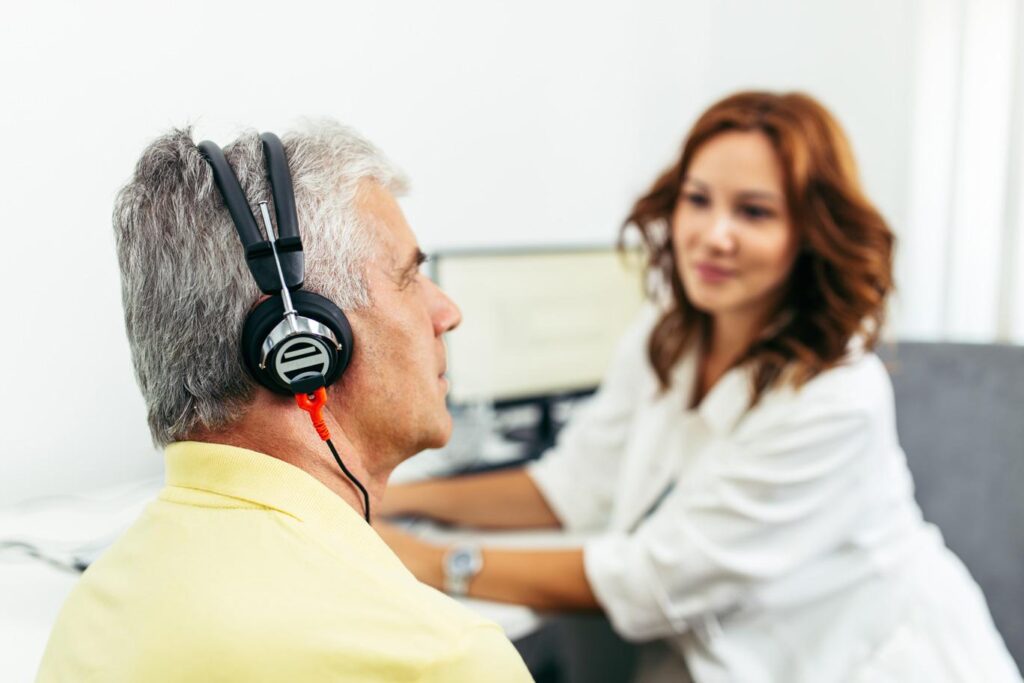 Audiology assistant testing for age-related hearing loss in man with yellow shirt