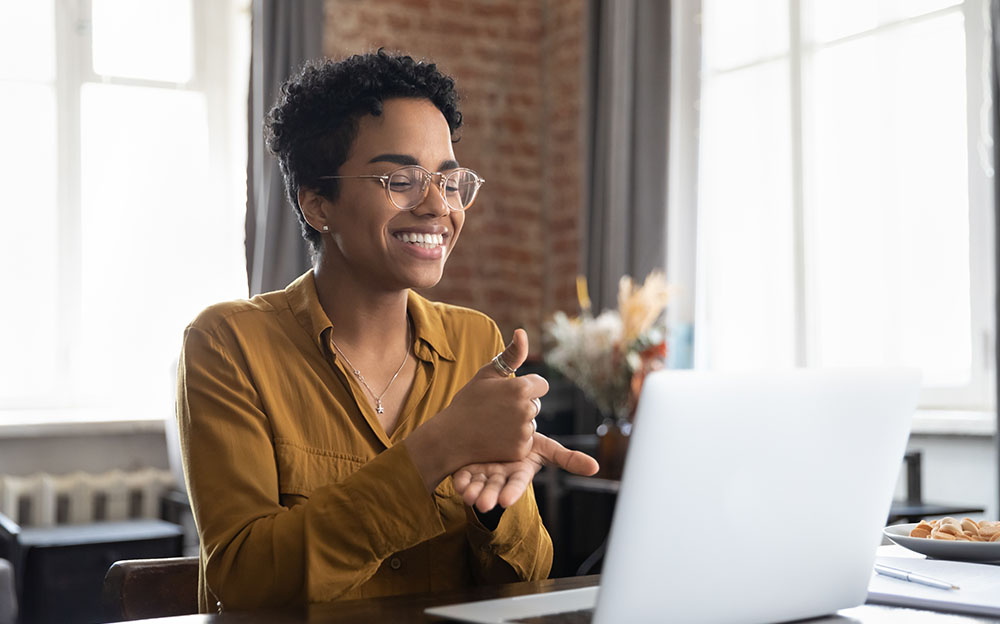 A person is chatting with someone on their computer in sign language while smiling.