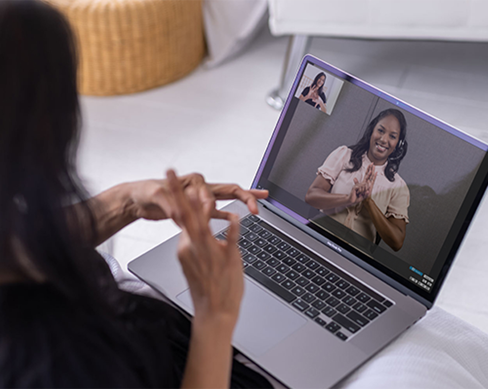 A person in front of a laptop uses sign language to communicate with an interpreter on the computer screen for Deaf employment support.