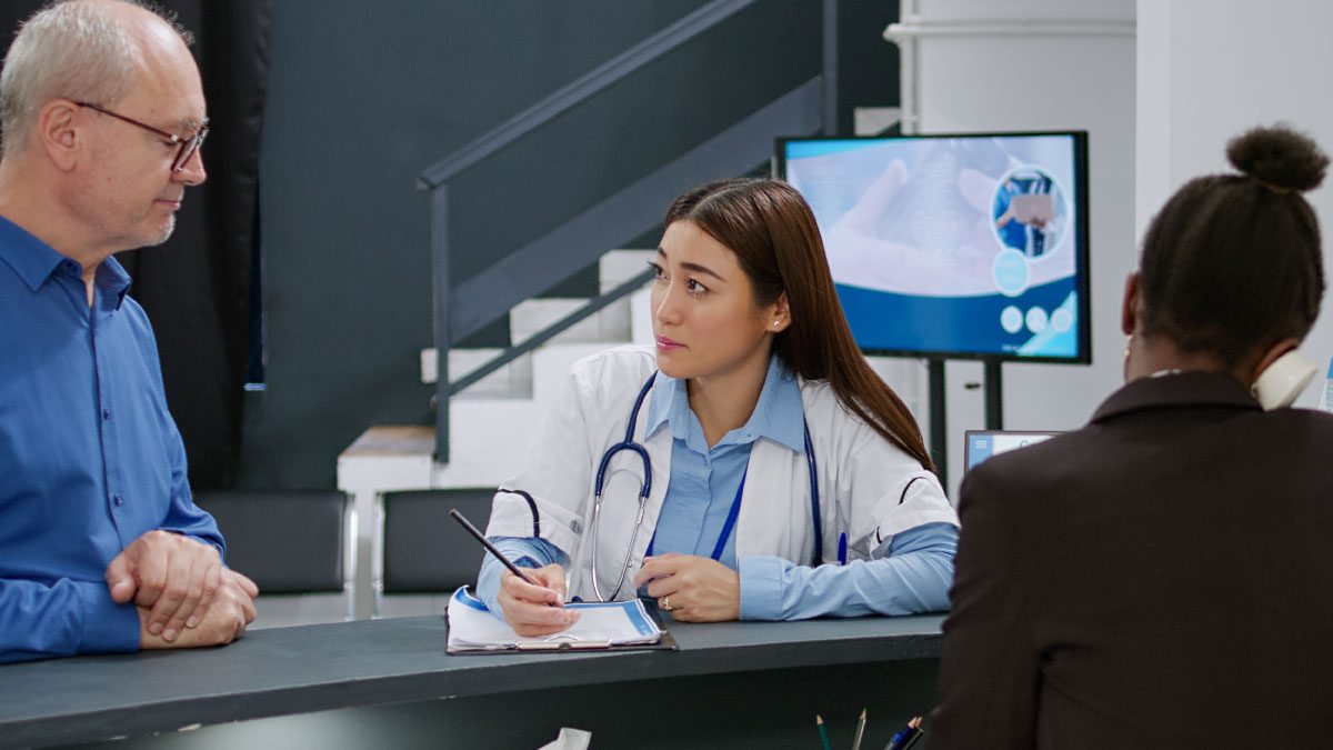 Male patient talking to female doctor at reception desk discussing hearing aid services